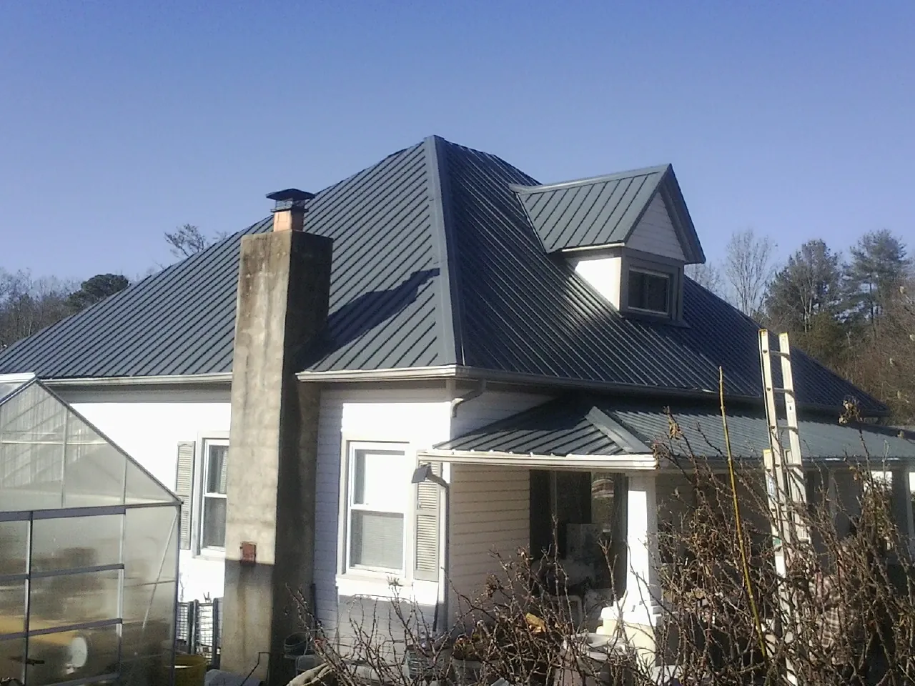 Dark blue standing seam metal roof on a white farmhouse with dormer — Slate & Tile Roof Repair by Roofing Brothers in Industry