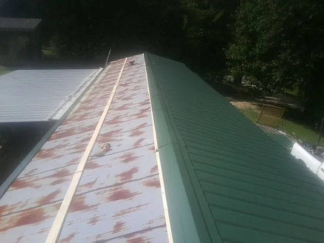 Old rusted panels beside newly installed green metal roofing — Wind Damage Roof Repair by Roofing Brothers in Industry